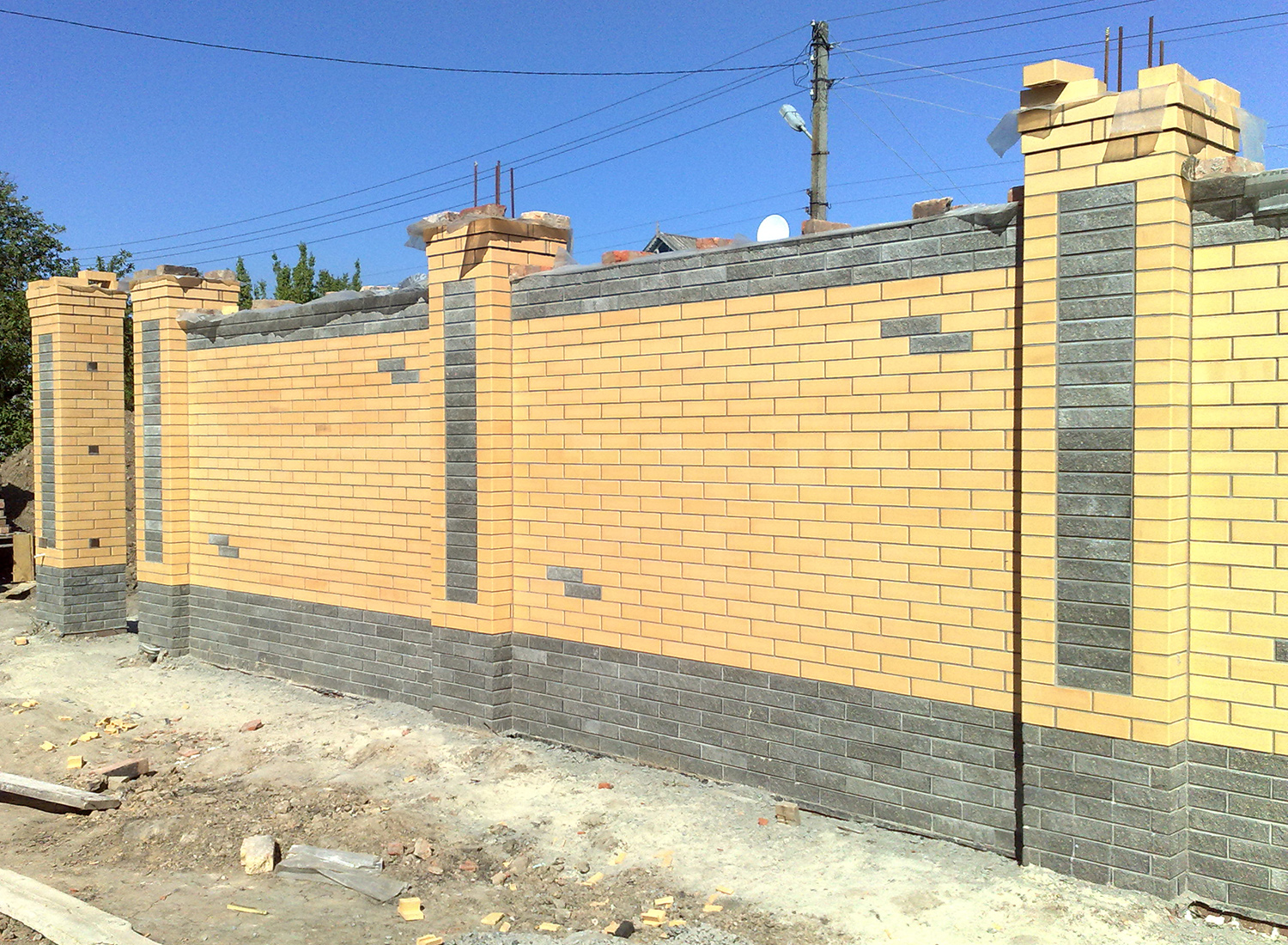 Забор из желтого кирпича на сером фундаменте